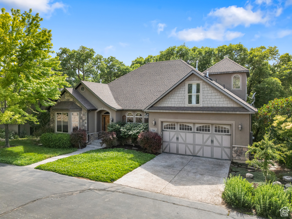 View of front of property featuring stone siding, a front yard, concrete driveway, an attached garage, and stucco siding