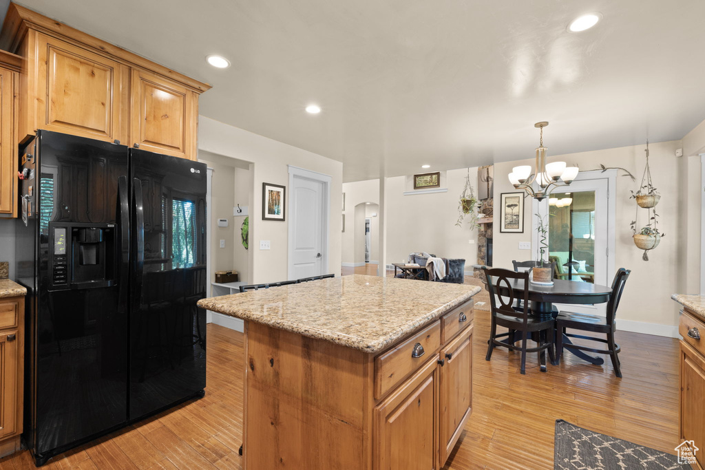 Kitchen featuring black refrigerator with ice dispenser, light wood-style floors, a kitchen island, a chandelier, and recessed lighting