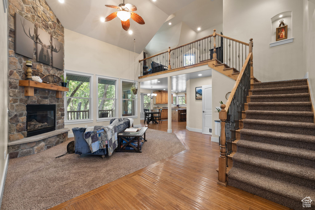 Living room with ceiling fan, wood-type flooring, a stone fireplace, high vaulted ceiling, and healthy amount of natural light