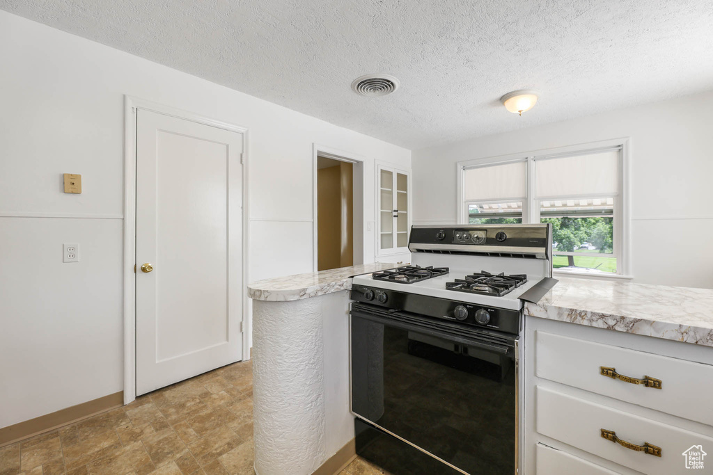 Kitchen with range with gas stovetop, light countertops, a textured ceiling, and white cabinets