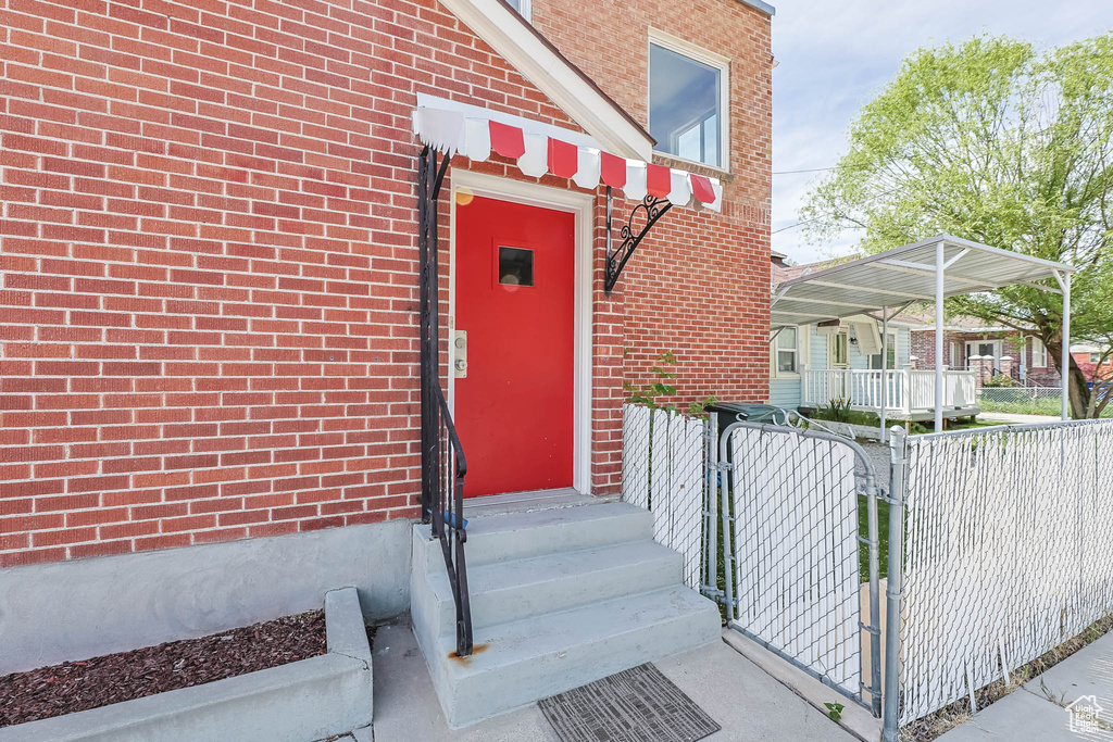 Doorway to property with a gate, a carport, and brick siding