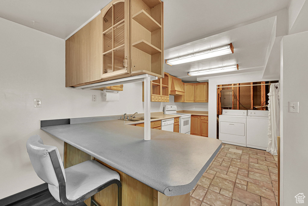 Kitchen featuring washer and dryer, open shelves, a peninsula, white appliances, and a breakfast bar