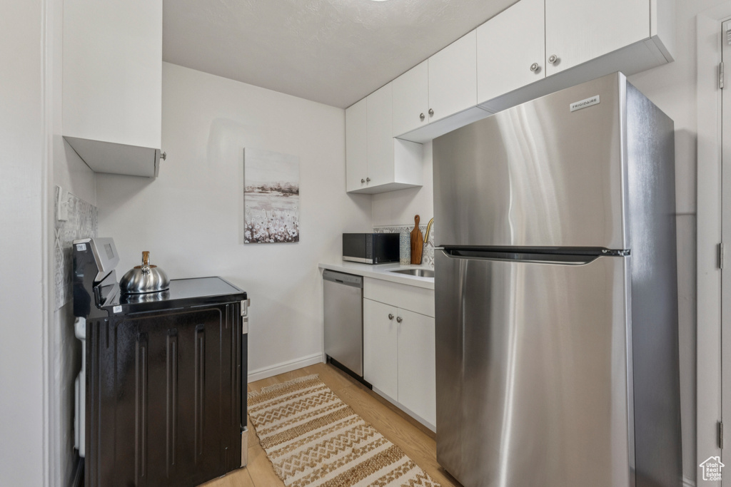 Kitchen with stainless steel appliances, light countertops, white cabinetry, and light wood-style floors