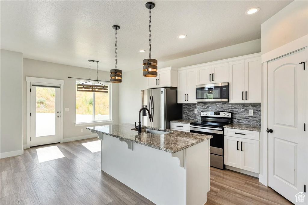 Kitchen with appliances with stainless steel finishes, a kitchen bar, recessed lighting, a center island with sink, and stone counters