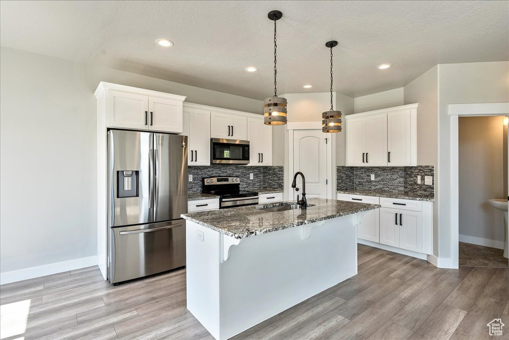 Kitchen featuring stainless steel appliances, tasteful backsplash, a breakfast bar area, light wood-style floors, and dark stone counters