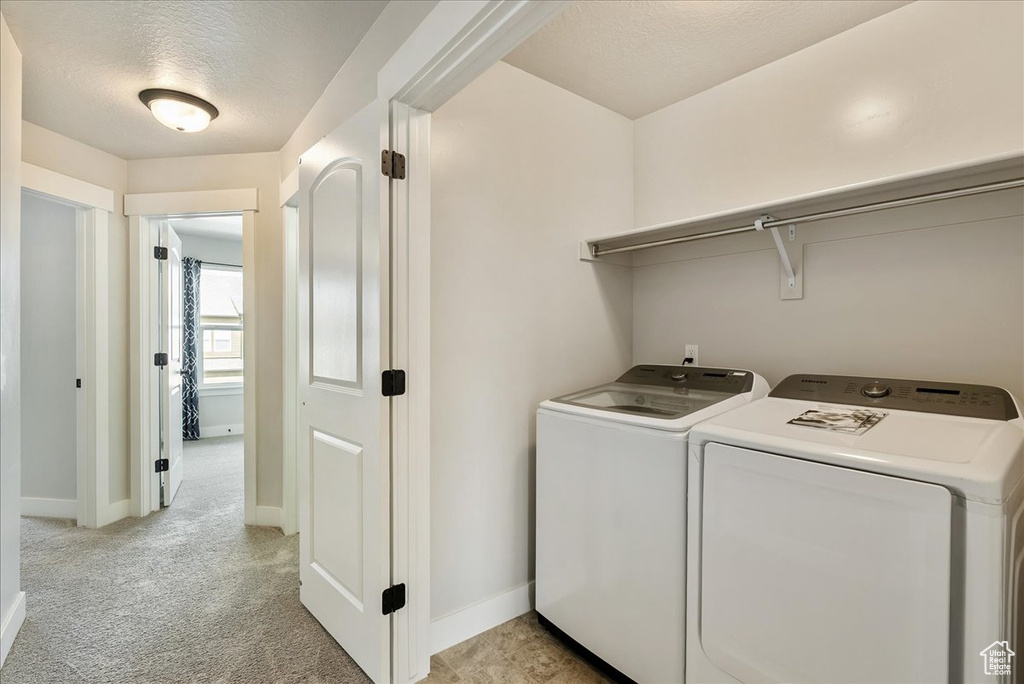 Laundry room featuring washer and clothes dryer, a textured ceiling, and light colored carpet