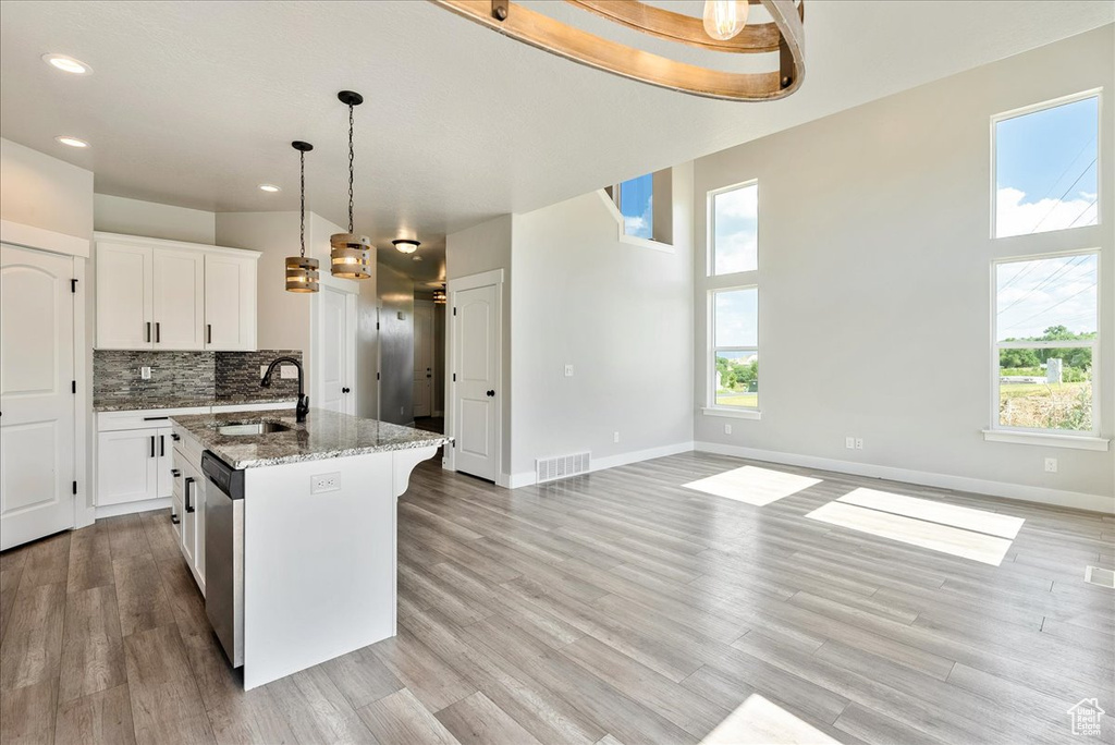 Kitchen with stainless steel dishwasher, an island with sink, light stone countertops, backsplash, and decorative light fixtures