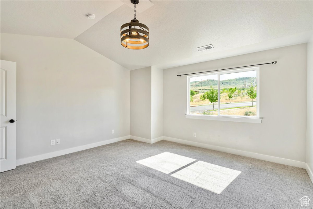 Empty room featuring a chandelier, vaulted ceiling, and light carpet