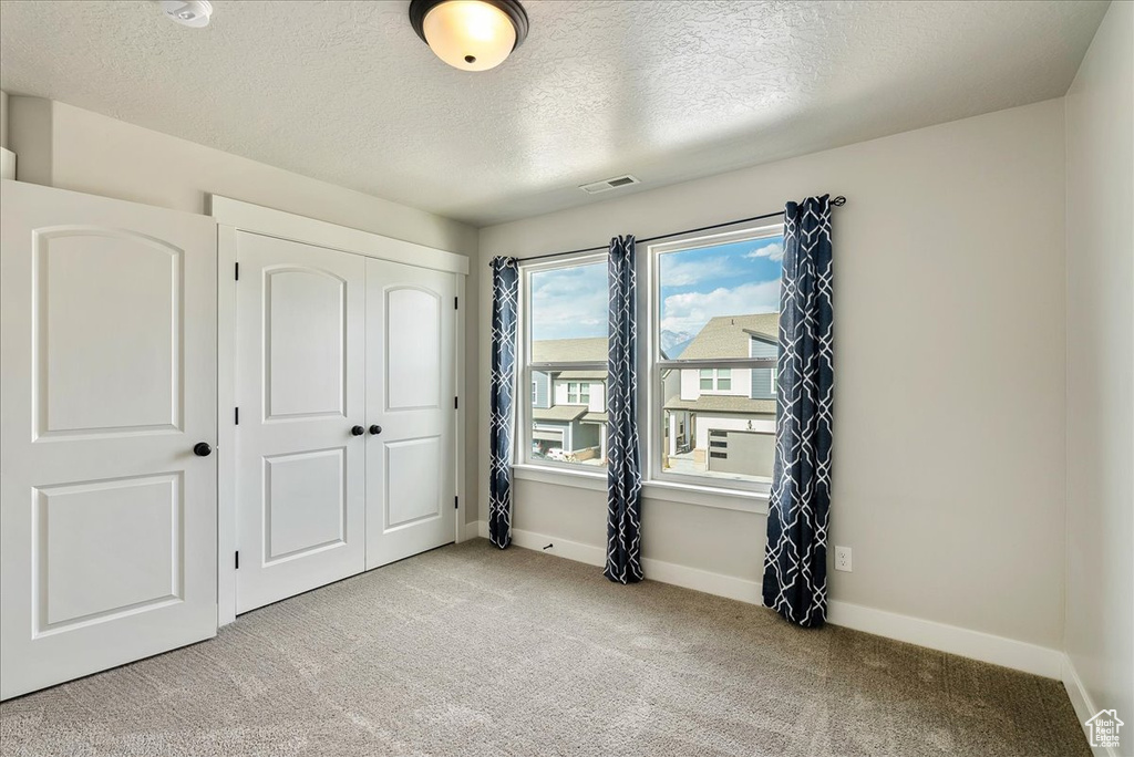Unfurnished bedroom featuring a textured ceiling, light carpet, and a closet