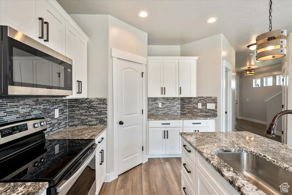 Kitchen with stainless steel appliances, light wood finished floors, white cabinets, backsplash, and recessed lighting