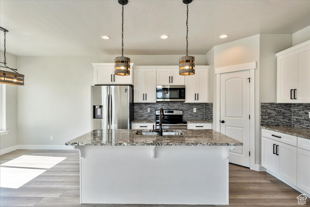 Kitchen featuring appliances with stainless steel finishes, dark stone counters, backsplash, recessed lighting, and an island with sink