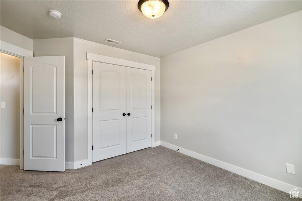 Unfurnished bedroom with carpet floors, a closet, and a textured ceiling