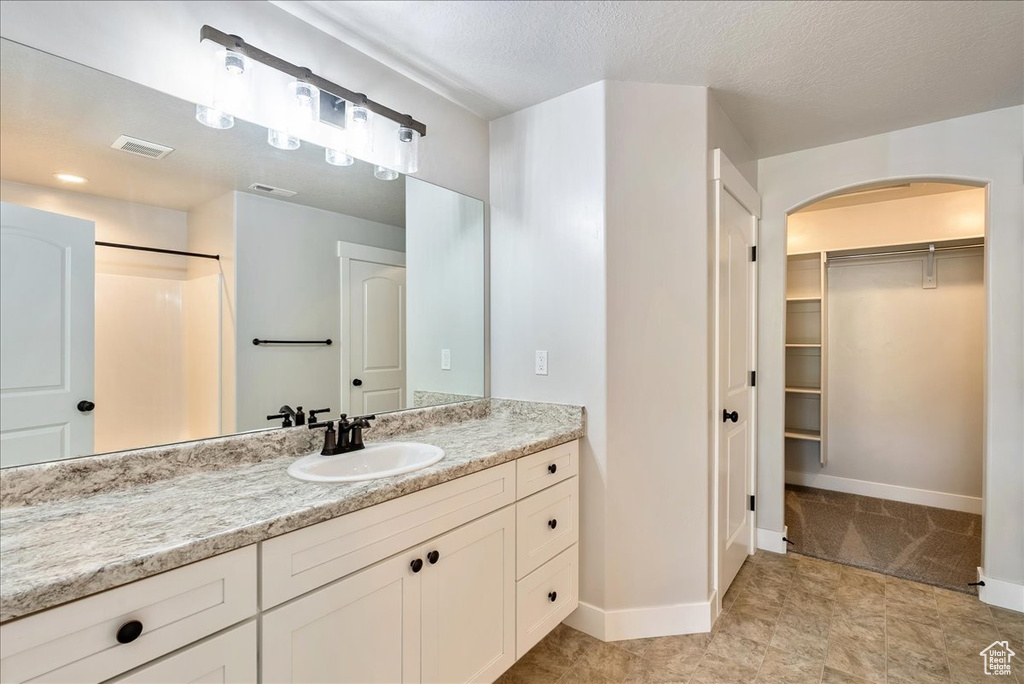 Bathroom featuring vanity, a spacious closet, a shower, and a textured ceiling