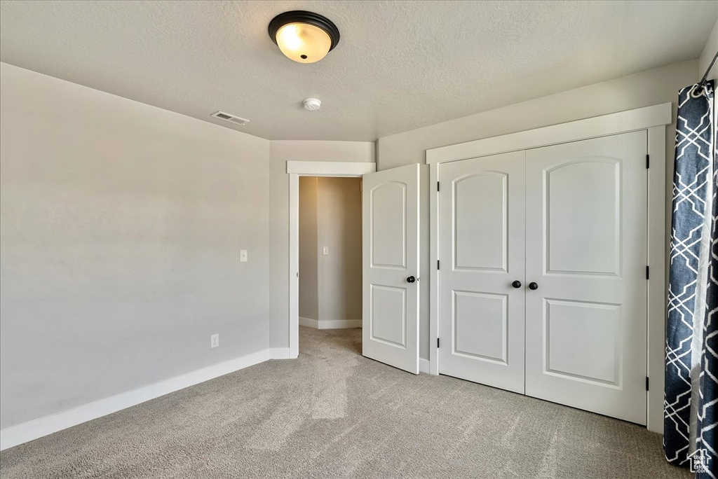 Unfurnished bedroom with light colored carpet, a closet, and a textured ceiling
