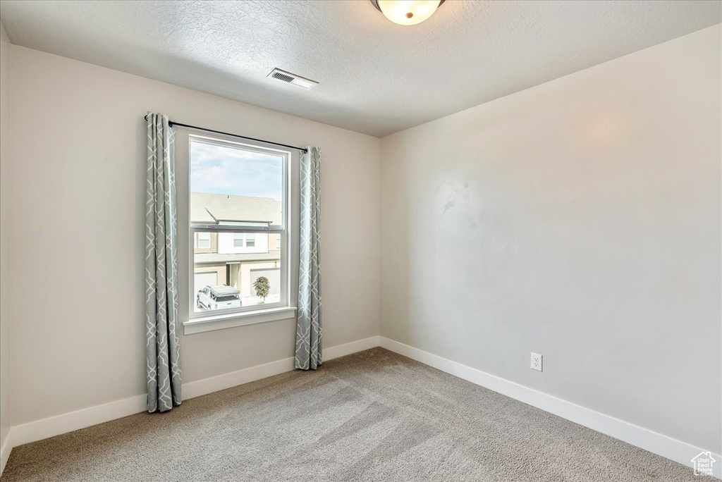 Carpeted empty room featuring a textured ceiling and baseboards