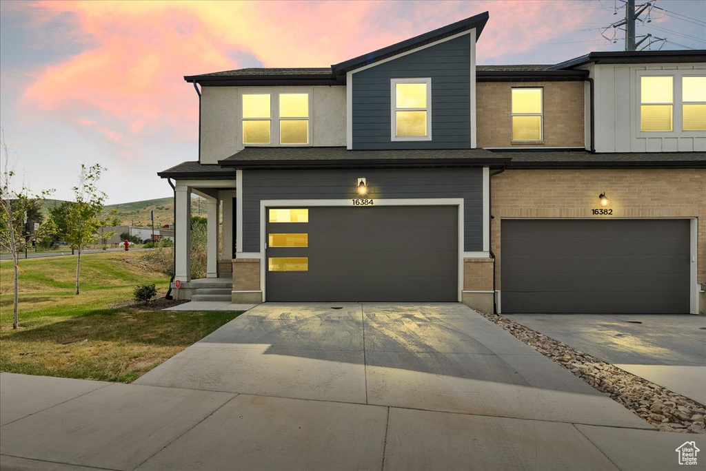View of front of property with a garage, driveway, brick siding, and a lawn