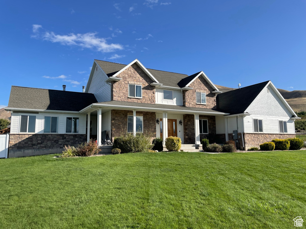 View of front of house with stone siding, a front yard, and covered porch