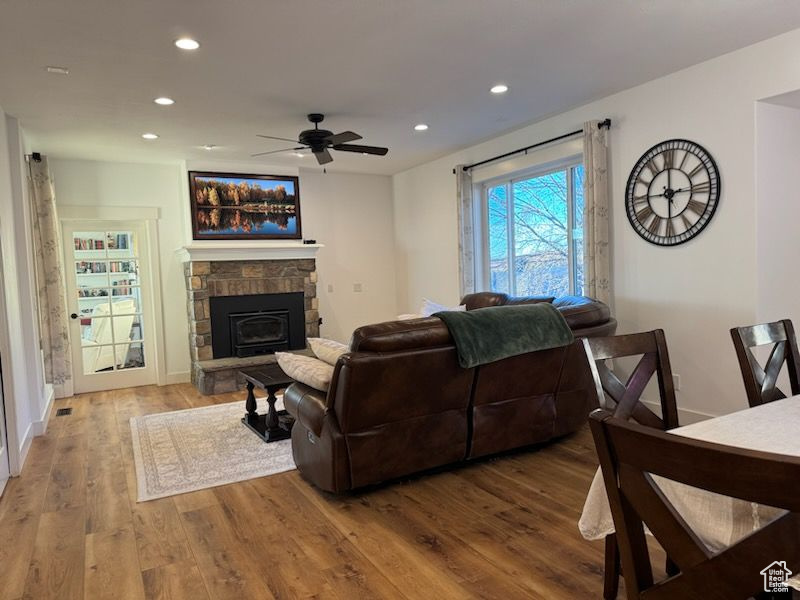 Living area featuring a ceiling fan, recessed lighting, a stone fireplace, and wood finished floors
