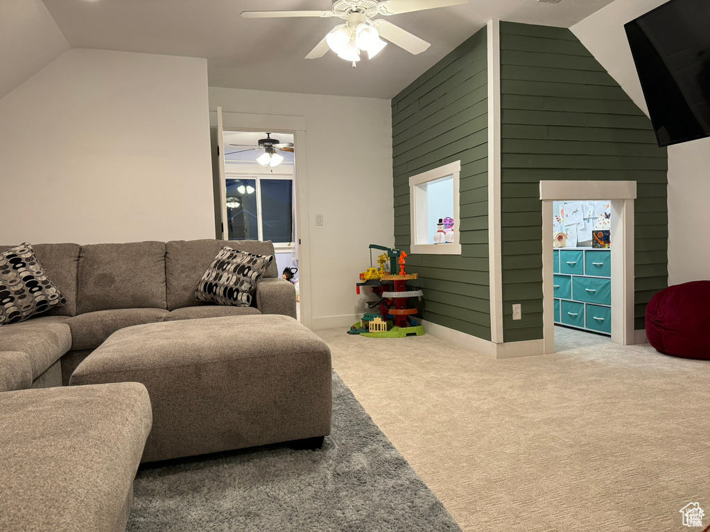 Carpeted living area with a ceiling fan, vaulted ceiling, and wooden walls