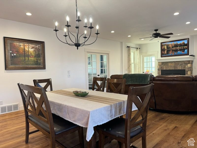 Dining room featuring recessed lighting, light wood finished floors, a chandelier, a stone fireplace, and ceiling fan