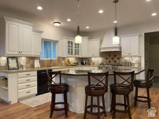 Kitchen with black dishwasher, custom exhaust hood, white cabinetry, recessed lighting, and a breakfast bar area