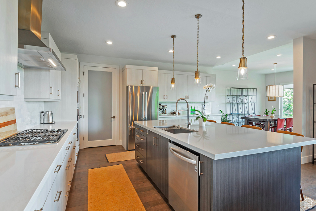Kitchen with wall chimney exhaust hood, appliances with stainless steel finishes, dark wood finished floors, light countertops, and recessed lighting