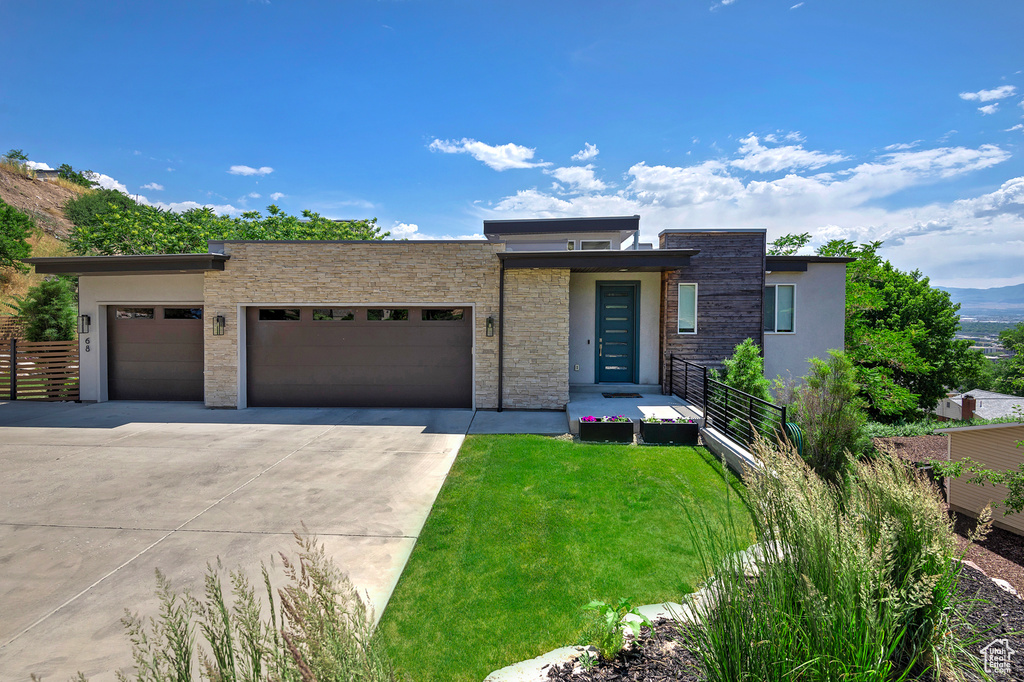 Contemporary house with a garage, concrete driveway, stone siding, a front lawn, and stucco siding