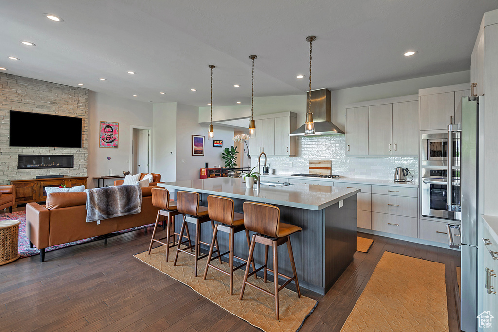 Kitchen featuring wall chimney exhaust hood, appliances with stainless steel finishes, open floor plan, dark wood-type flooring, and light countertops