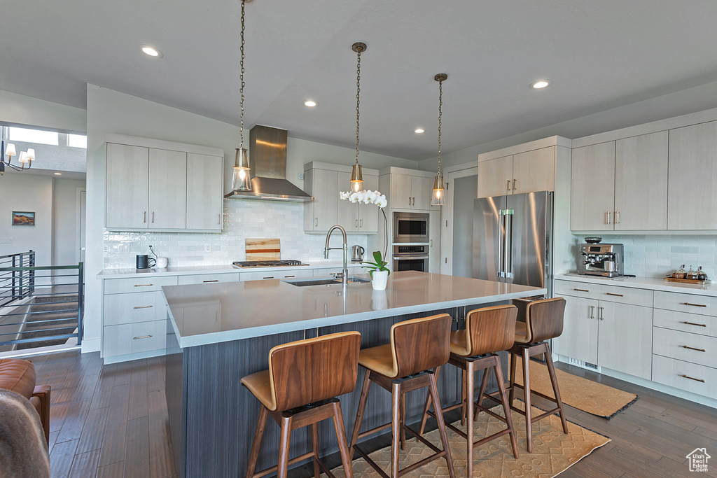 Kitchen featuring wall chimney range hood, stainless steel appliances, a breakfast bar area, backsplash, and a kitchen island with sink