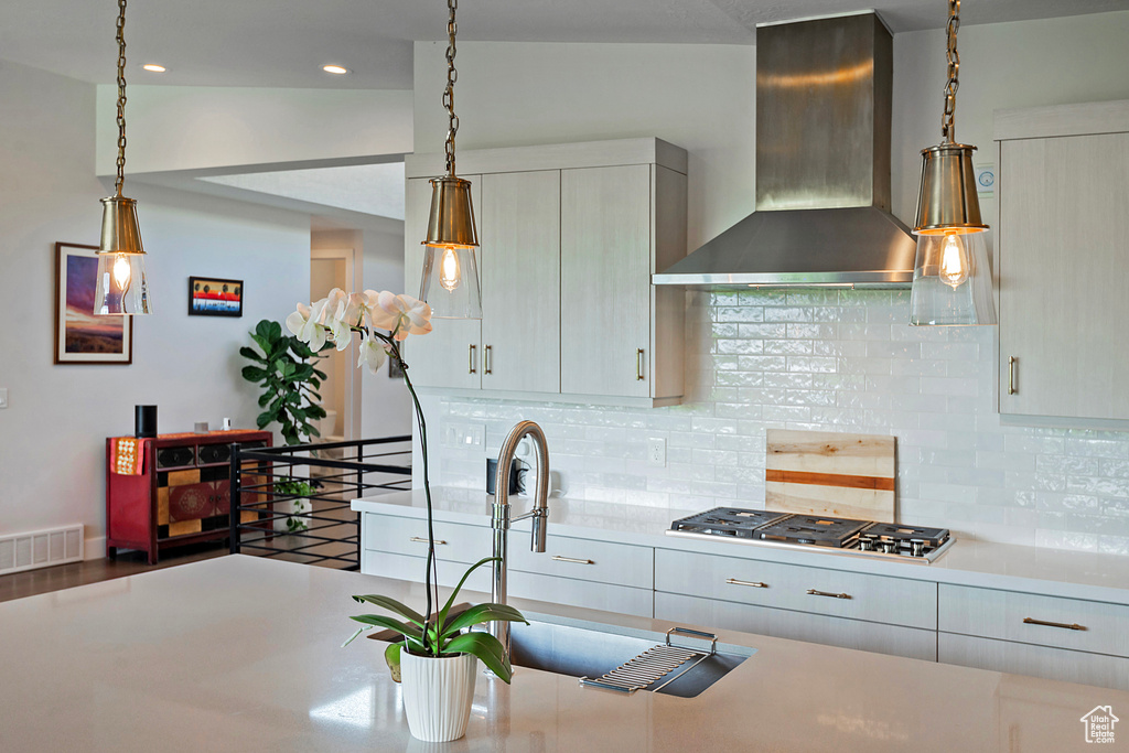 Kitchen with wall chimney range hood, stainless steel gas cooktop, light countertops, decorative backsplash, and recessed lighting