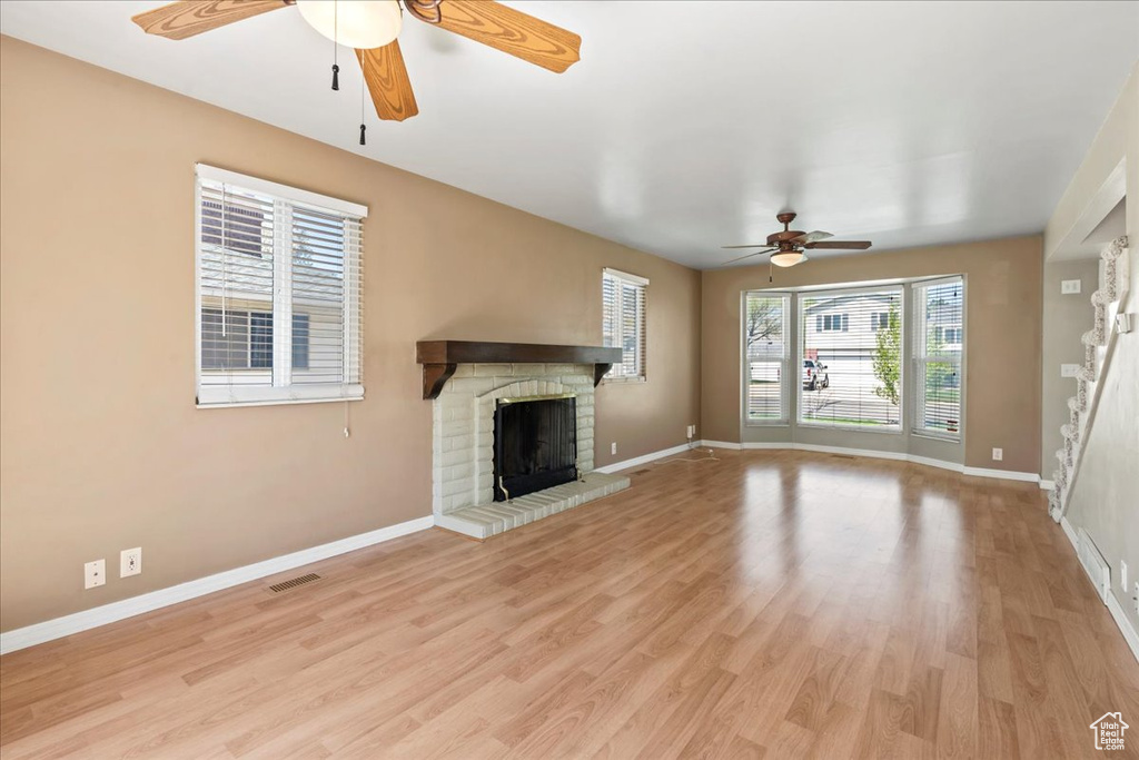 Unfurnished living room with a ceiling fan, a fireplace, and light wood-type flooring
