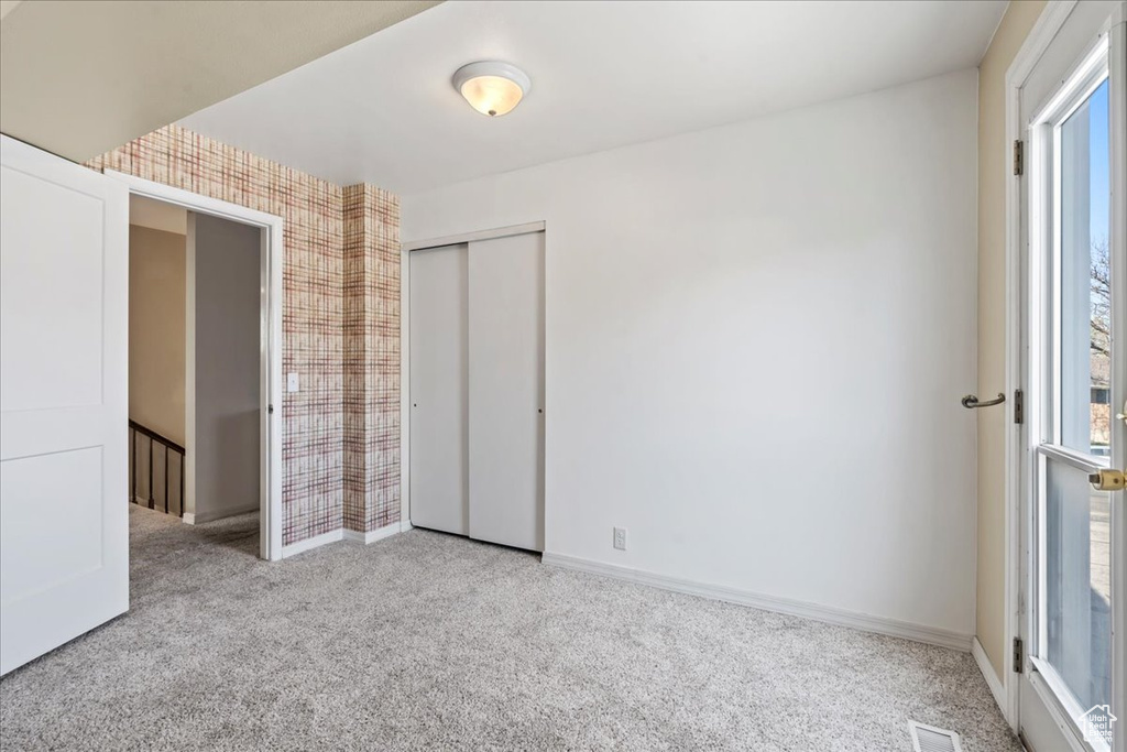 Unfurnished bedroom with carpet floors, multiple windows, a closet, and wallpapered walls