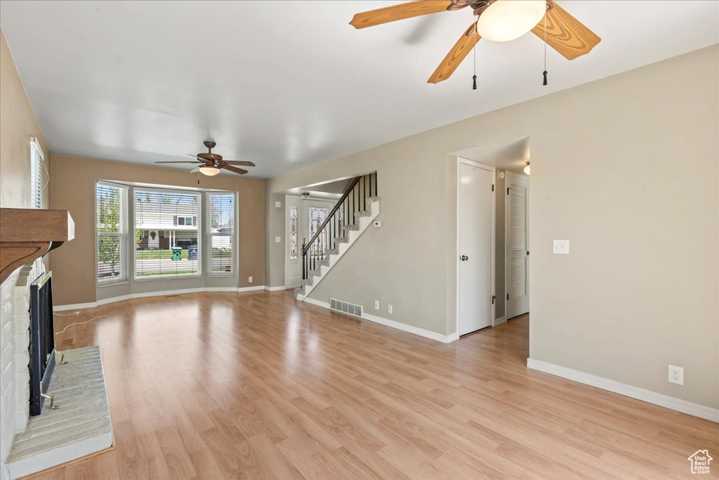 Unfurnished living room with a ceiling fan, stairs, light wood finished floors, and a fireplace