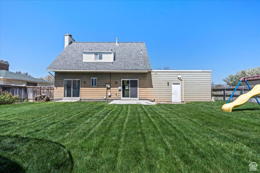 Back of property with a fenced backyard, a chimney, a playground, and a shingled roof