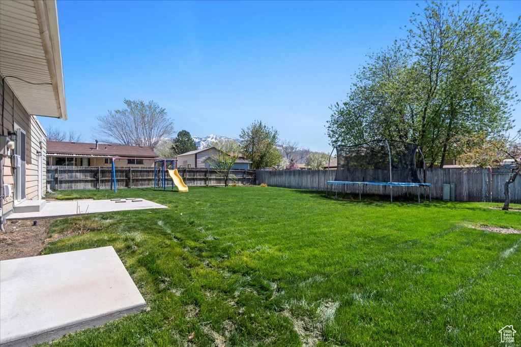 Fenced backyard with a trampoline, a playground, and a patio