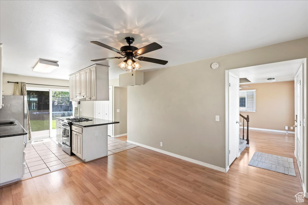 Kitchen featuring stainless steel appliances, dark countertops, ceiling fan, and light wood-type flooring