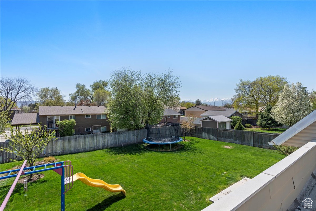 Fenced backyard with a trampoline, a playground, and a residential view
