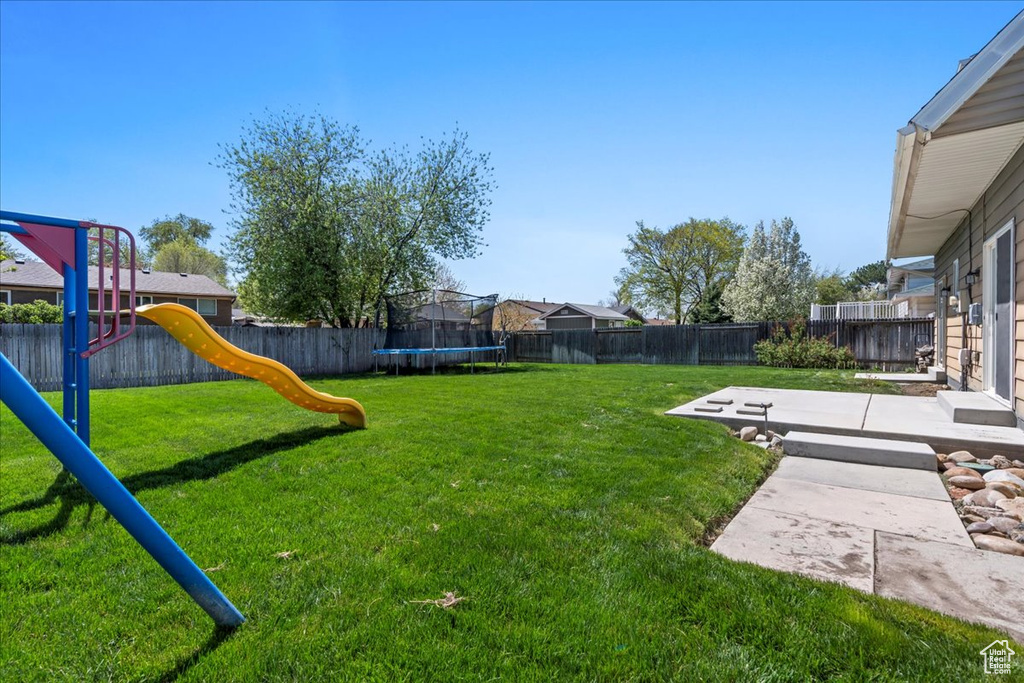 Fenced backyard with a trampoline, a playground, and a patio