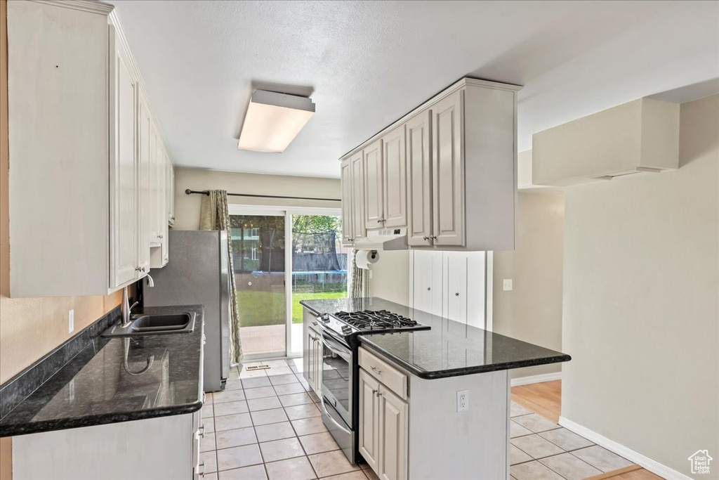 Kitchen with stainless steel range with gas stovetop, light tile patterned flooring, and dark stone counters
