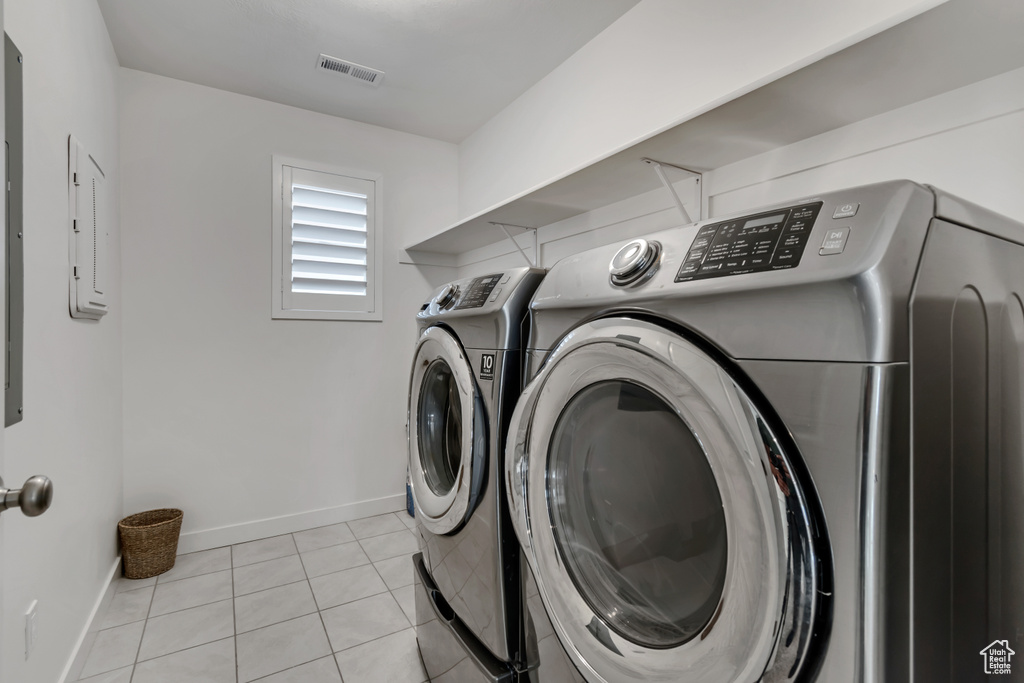Laundry room featuring washer and dryer, light tile patterned floors, and electric panel