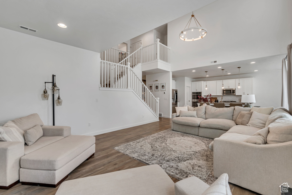 Living area with stairs, a chandelier, wood finished floors, a high ceiling, and recessed lighting