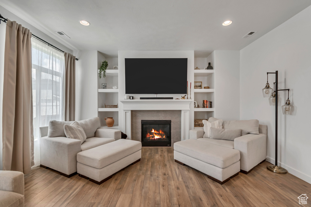 Living room featuring a tile fireplace, wood finished floors, built in shelves, and recessed lighting