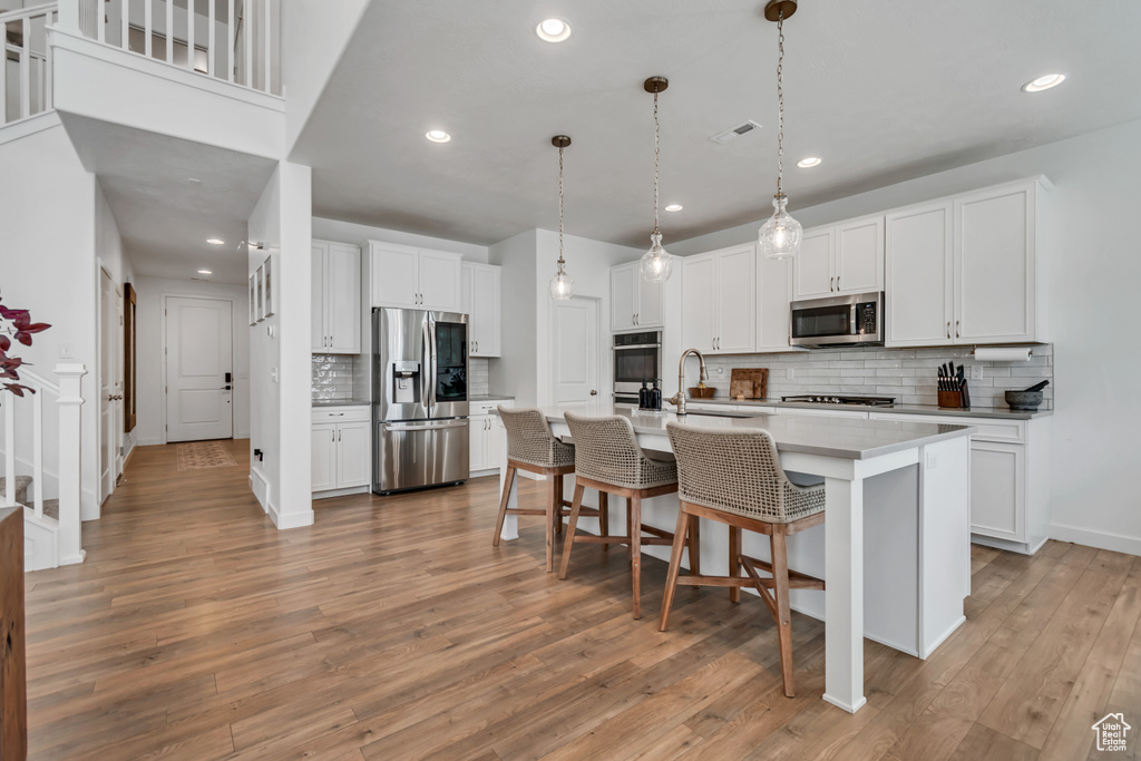 Kitchen with stainless steel appliances, decorative backsplash, recessed lighting, light wood finished floors, and white cabinets