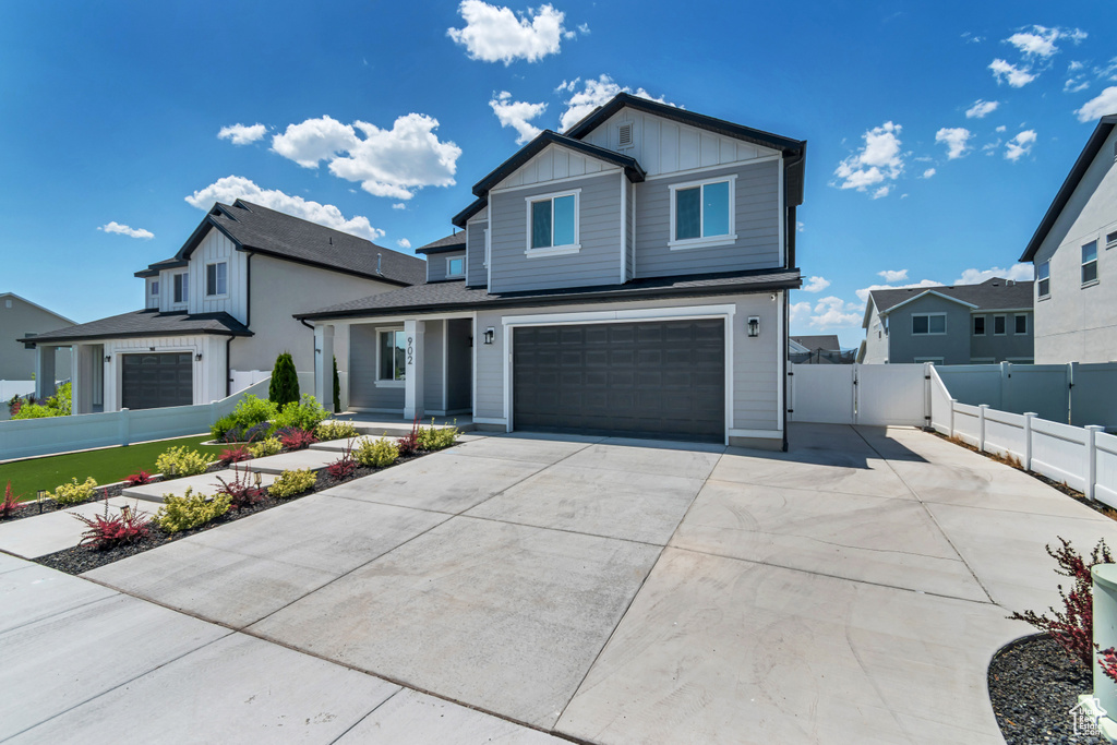 View of front of property with board and batten siding, an attached garage, driveway, and a gate