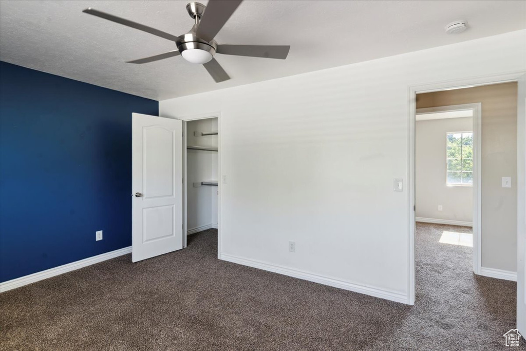 Unfurnished bedroom with dark colored carpet, a walk in closet, ceiling fan, and a closet