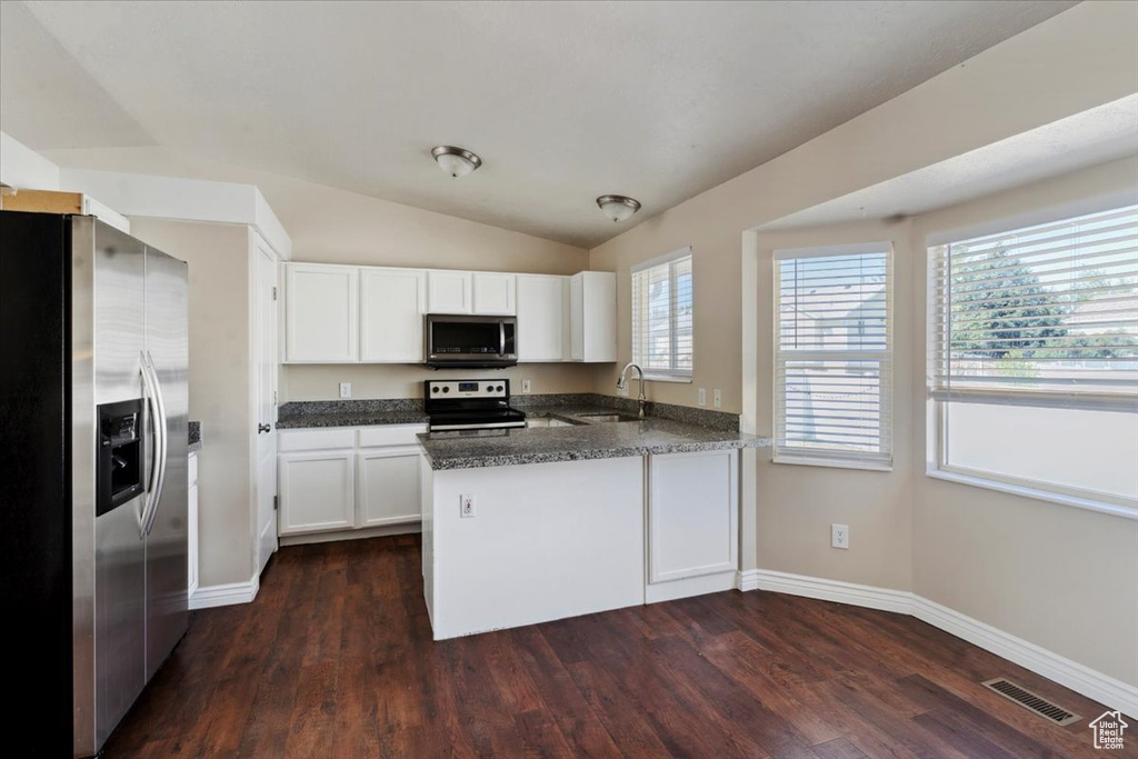 Kitchen featuring stainless steel appliances, a peninsula, white cabinetry, dark wood-type flooring, and lofted ceiling