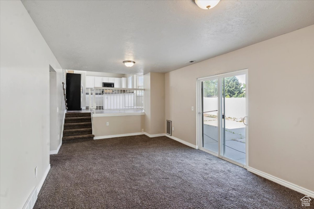 Unfurnished living room featuring dark carpet and stairway