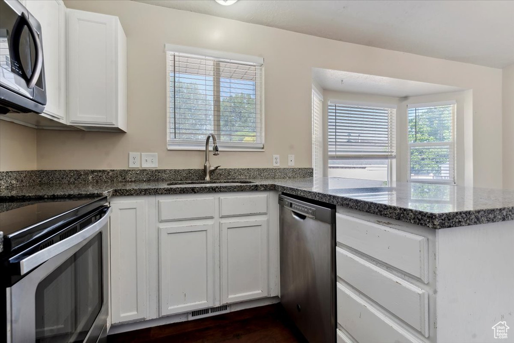 Kitchen featuring stainless steel appliances, dark stone countertops, a peninsula, and white cabinetry