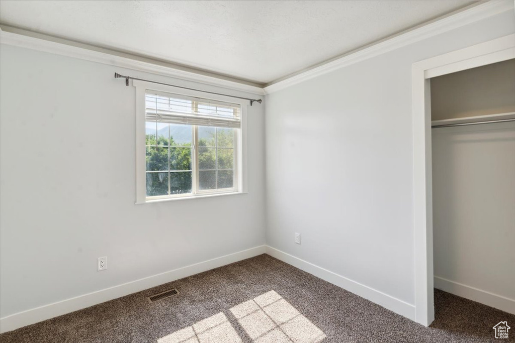 Unfurnished bedroom with dark carpet, a closet, and ornamental molding
