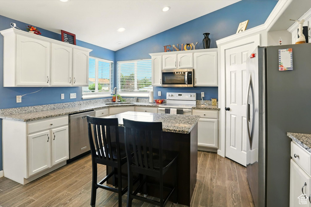 Kitchen featuring appliances with stainless steel finishes, vaulted ceiling, white cabinetry, wood finished floors, and a kitchen island